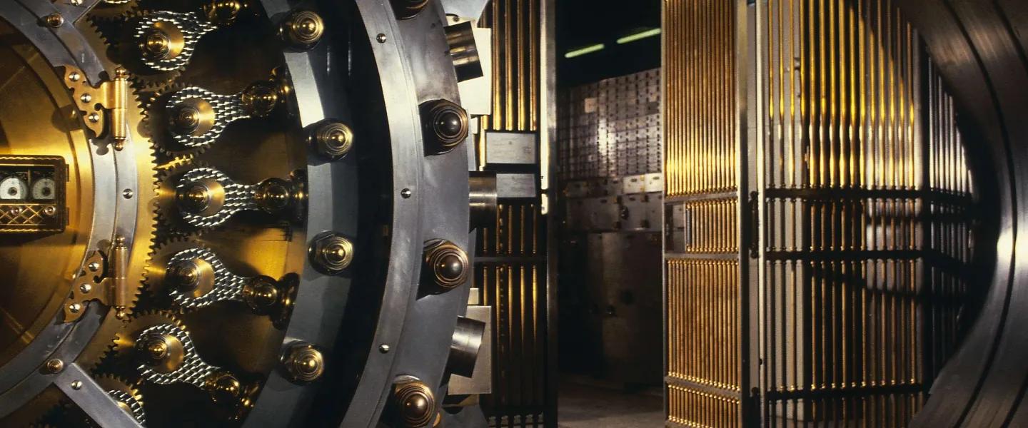 Open circular steel-and-gold bank vault door leading into a secure storage room