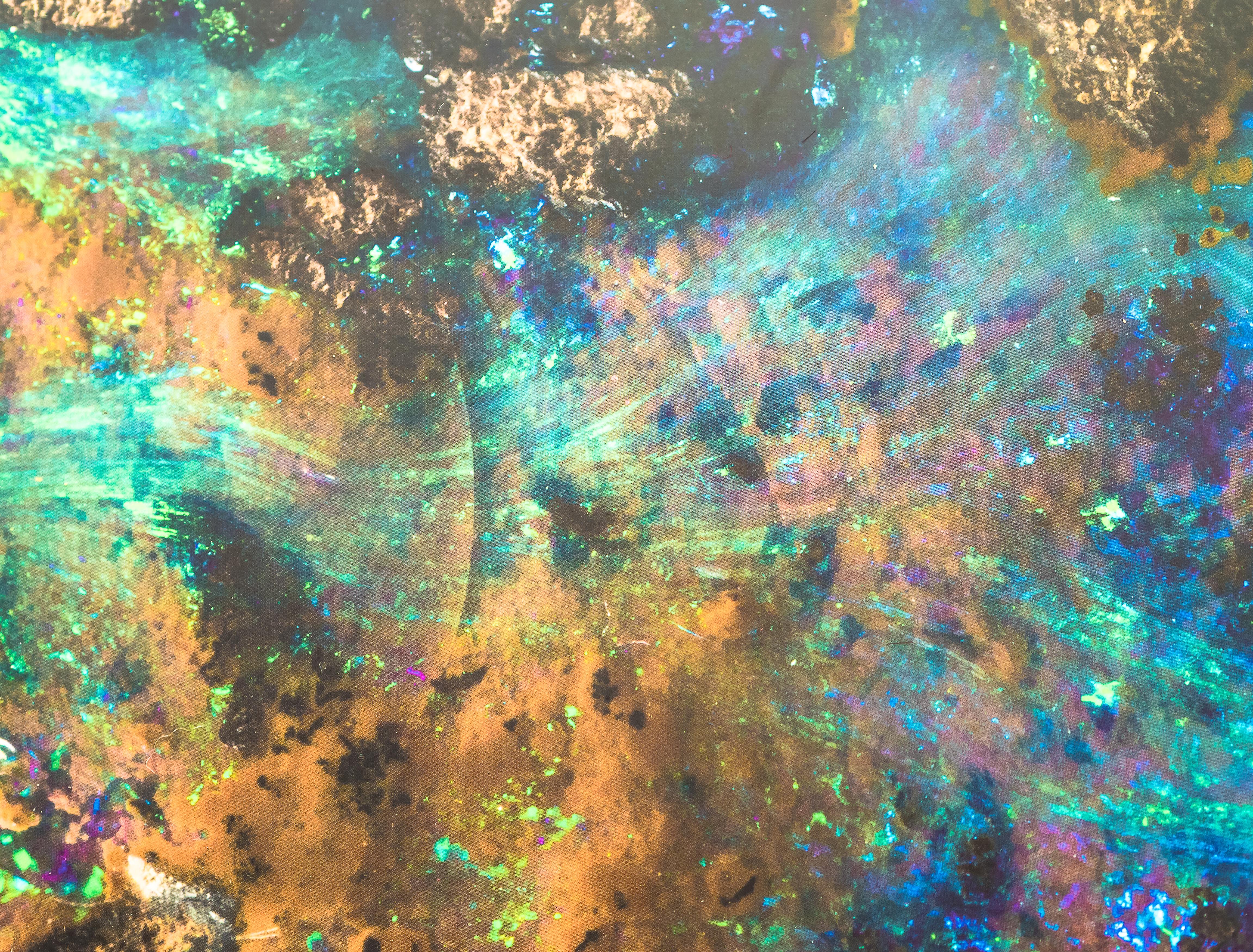 Macro photograph of Queensland boulder opal showing iridescent blue, green, violet and gold colour across brown ironstone