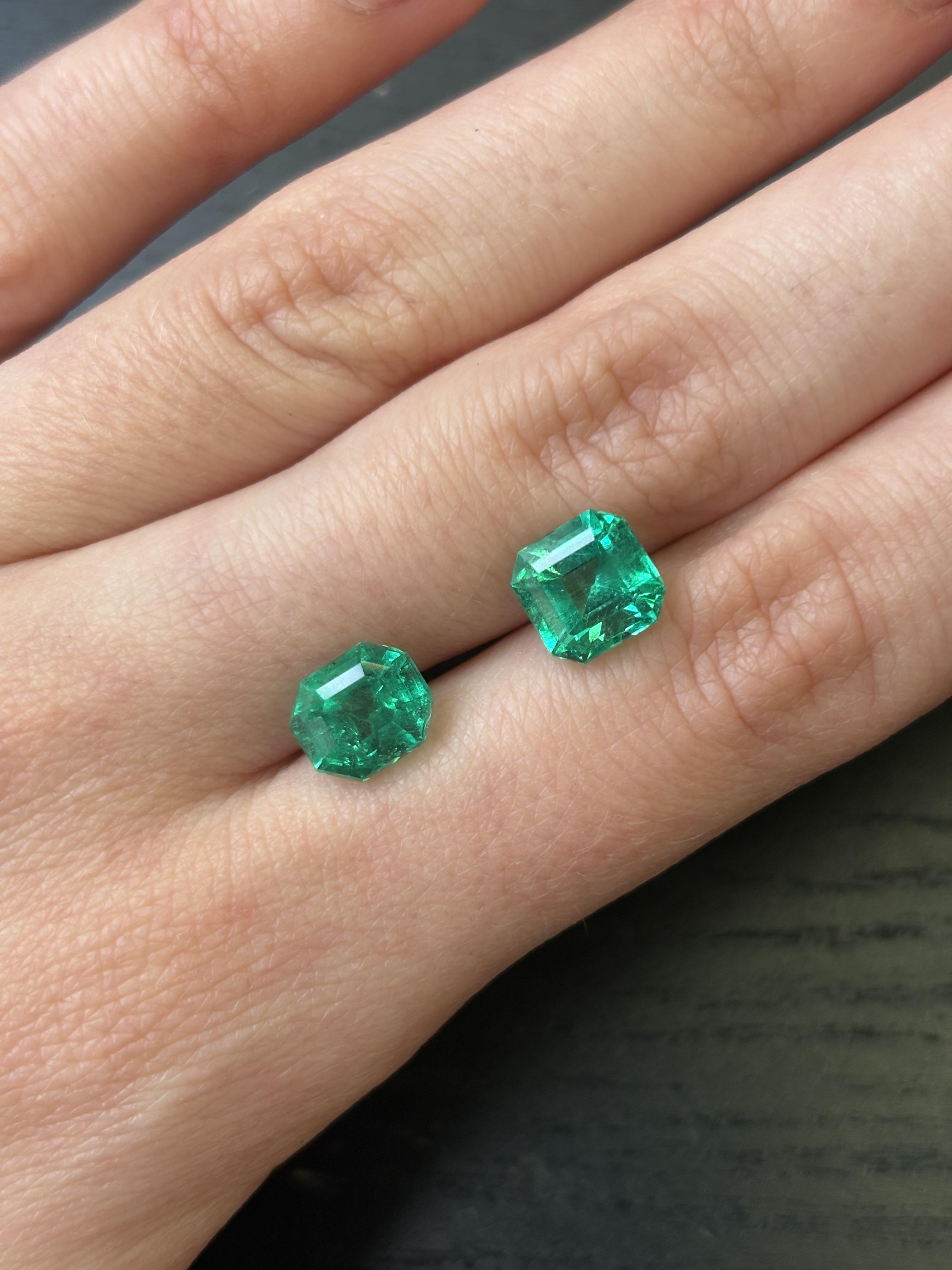 Two cut emerald gemstones resting on fingers, displaying vivid green colour and octagonal-style cuts.