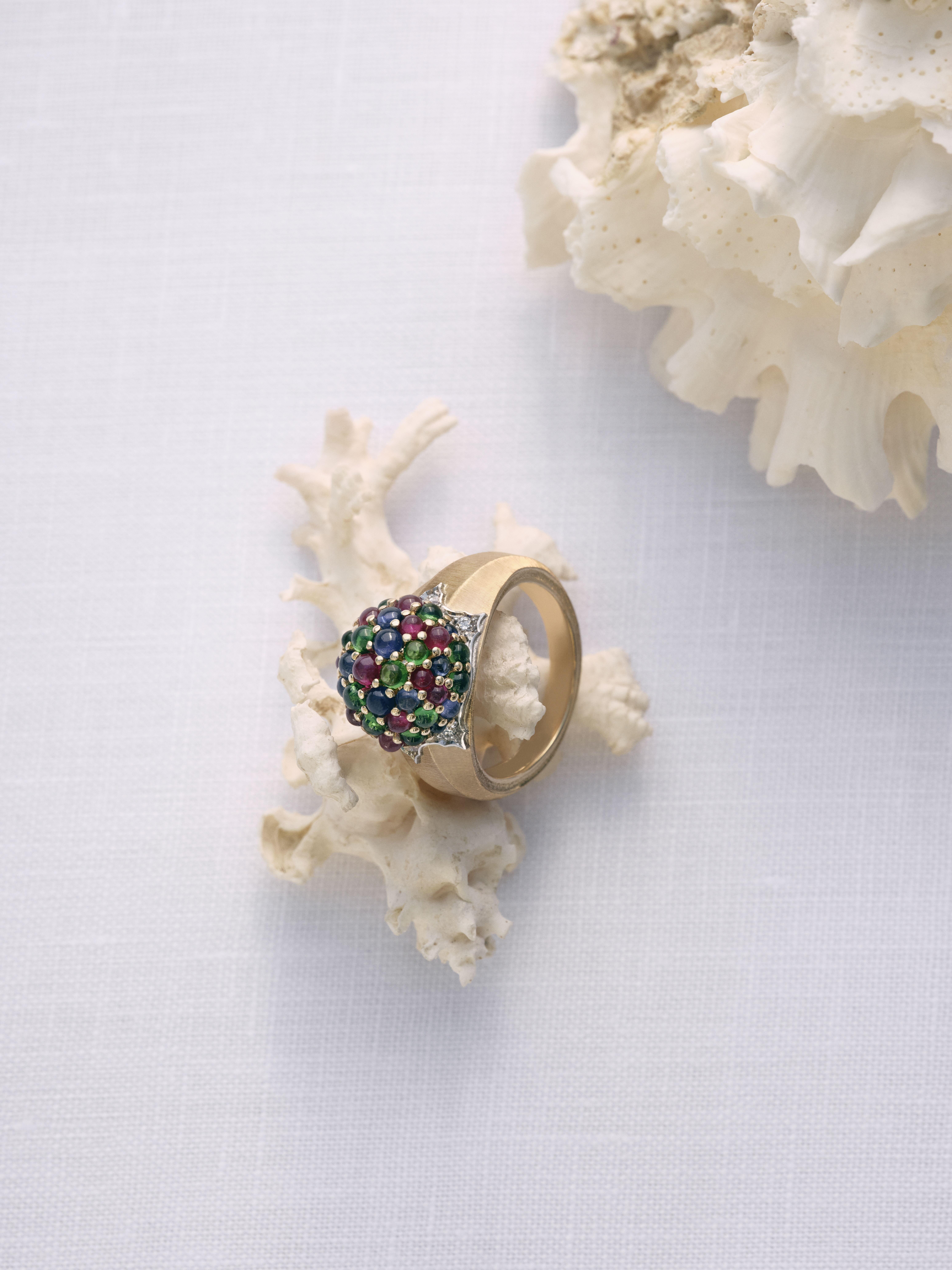 Buccellati Muse collection ring with multicoloured gemstones and textured gold detailing displayed on coral-inspired props.