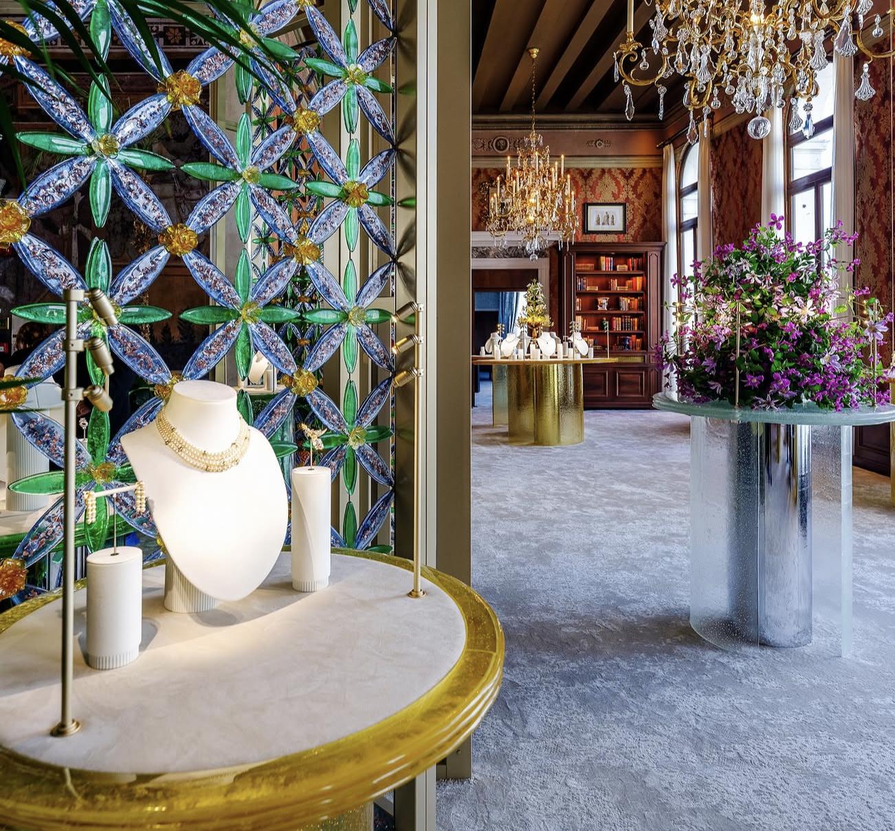 Tiffany jewellery displayed beside a wall of blue and green glass flowers, chandeliers and a large arrangement of purple flowers