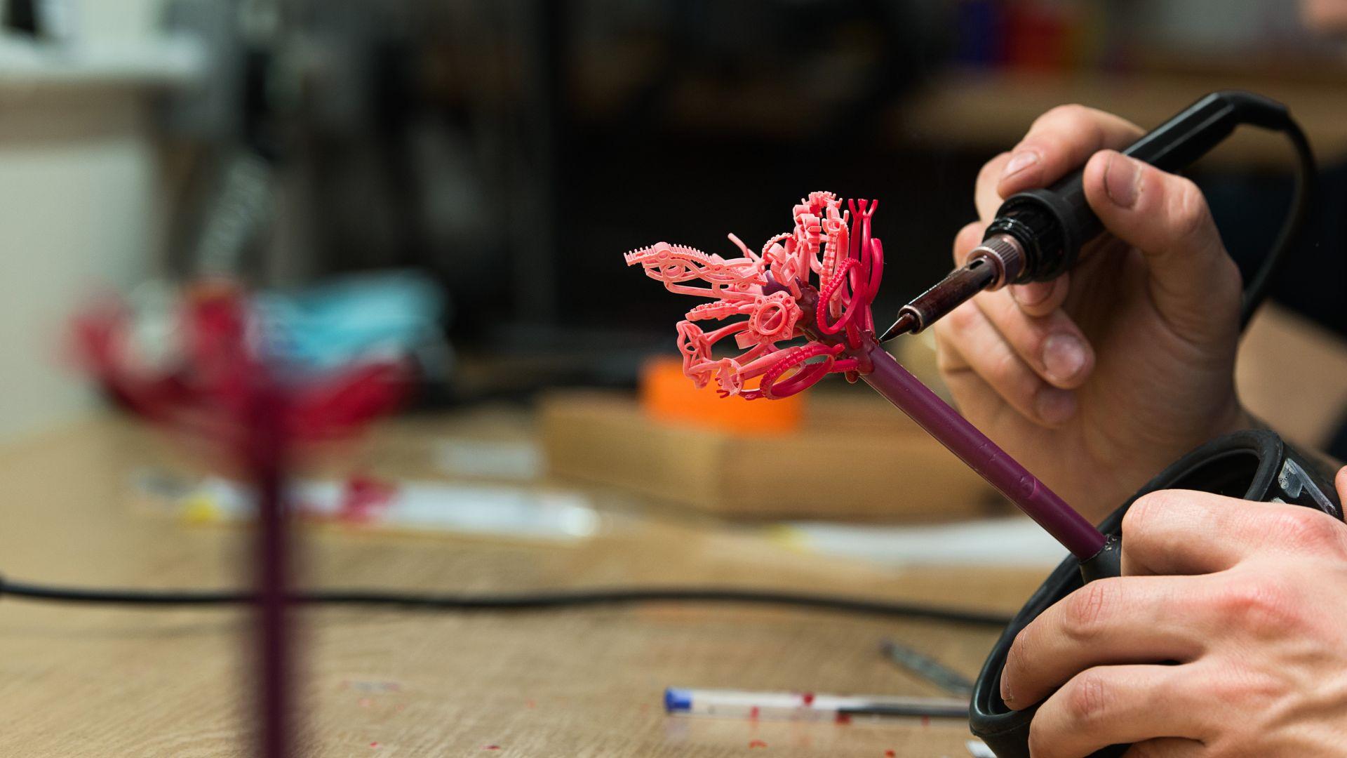 Craftsperson working on a tree of pink wax jewellery models with a heated tool in a workshop.