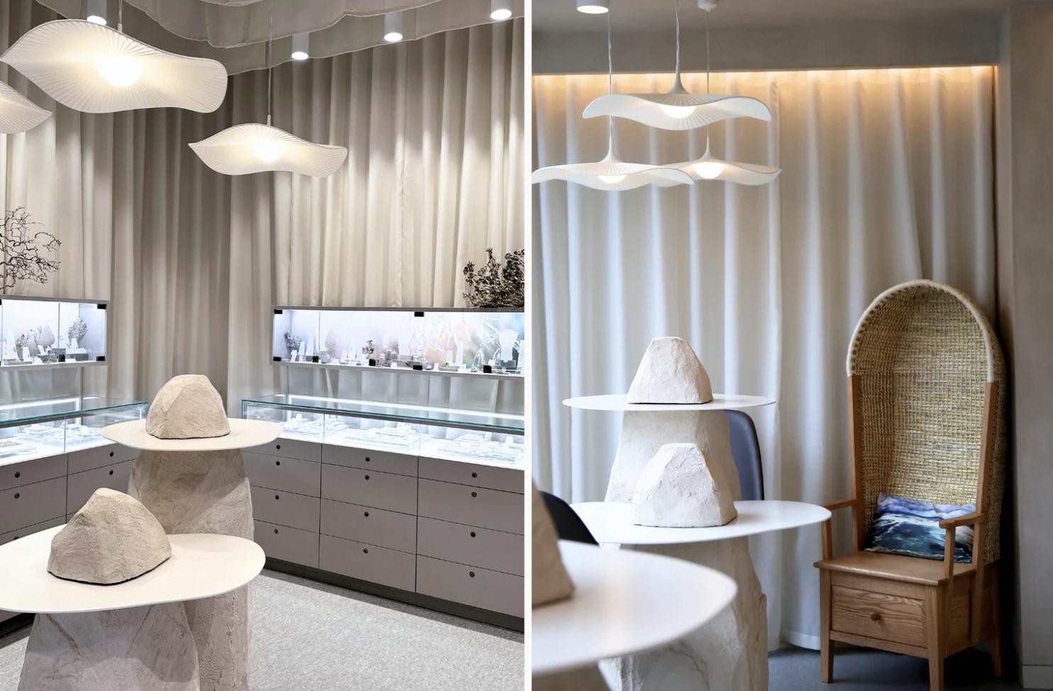 Two views of Sheila Fleet Jewellery’s upstairs gallery, featuring illuminated jewellery displays, pale sculptural tables, wave-shaped pendant lights and a high-backed wooden chair