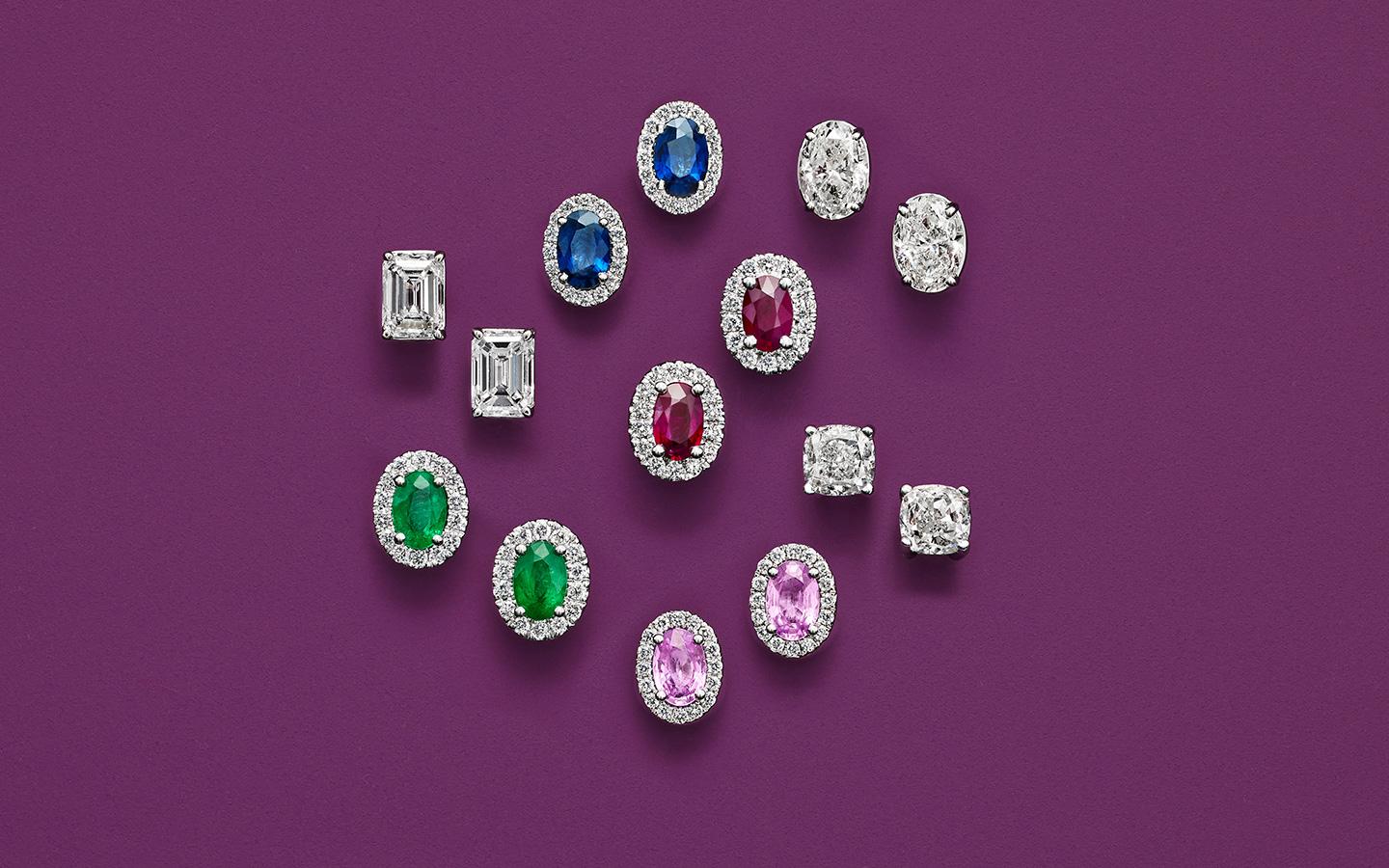 Blue, pink, red, green and white gemstone studs with diamond halos arranged on a purple background.