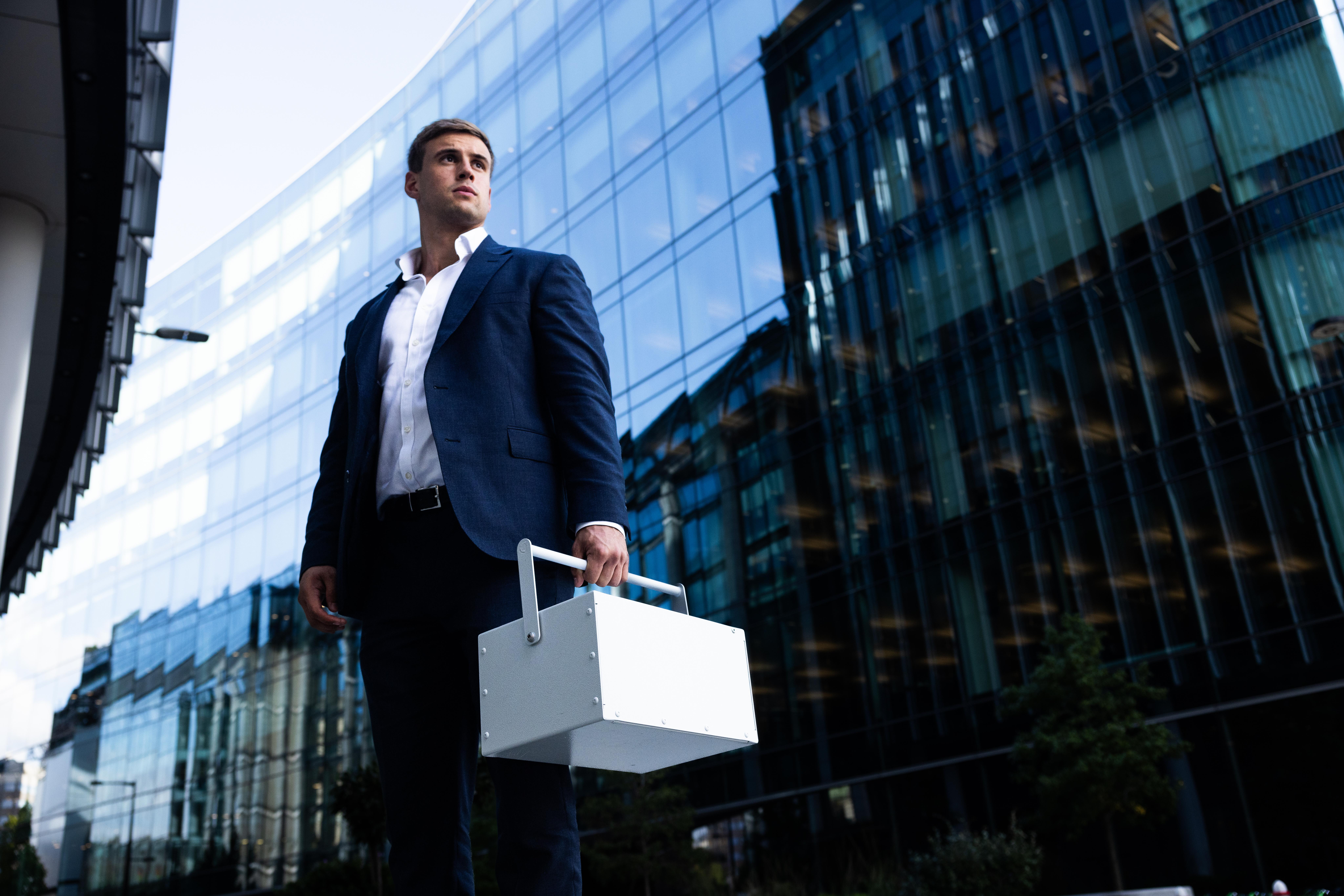 An Ultra-Vault representative carrying a portable vault box outside a modern office building, illustrating the company’s secure collection and delivery service for valuables.